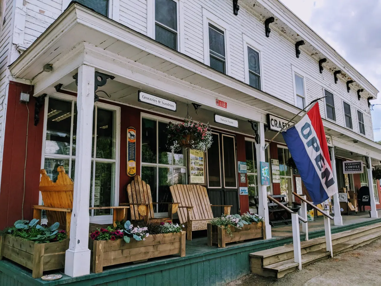 The porch of a Vermont general store — Adirondack chairs, flower boxes, and an OPEN flag